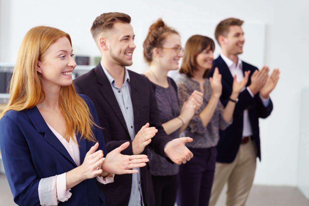 Row of impressed young business co-workers clapping a colleague work