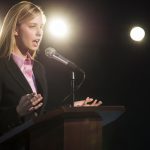 young-businesswoman-giving-speech-podium-auditorium